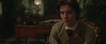 Movie still from “Enola Holmes 2” (2022), directed by Harry Bradbeer – A man in a suit and tie sitting in front of a lamp; Close Up shot, Over the shoulder angle