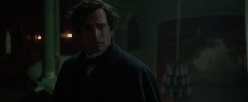 Movie still from “Enola Holmes 2” (2022), directed by Harry Bradbeer – A man standing in a dark room wearing a coat and tie; Close Up shot, Over the shoulder angle