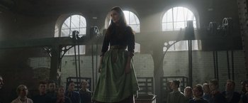 Movie still from “Enola Holmes 2” (2022), directed by Harry Bradbeer – A woman standing in front of a group of people in a room; Wide shot, Low angle