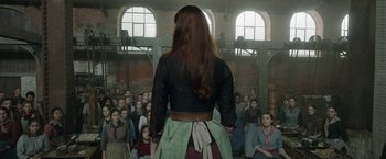 Movie still from “Enola Holmes 2” (2022), directed by Harry Bradbeer – A group of people standing in front of a woman; Wide shot, Over the shoulder angle