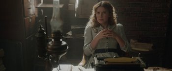 Movie still from “Enola Holmes 2” (2022), directed by Harry Bradbeer – A woman sitting at a table in a dimly - lit room; Medium shot, Over the shoulder angle