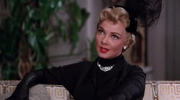 Movie still from “Kiss Me Kate” (1953), directed by George Sidney – A woman with blonde hair and red lipstick wearing a black dress; Close Up shot, Over the shoulder angle