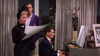 Movie still from “Kiss Me Kate” (1953), directed by George Sidney – A group of people standing around a piano; Medium shot, Over the shoulder angle