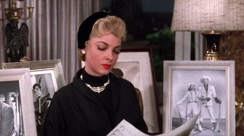 Movie still from “Kiss Me Kate” (1953), directed by George Sidney – A woman sitting in a chair reading a newspaper; Close Up shot, High angle