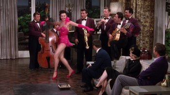 Movie still from “Kiss Me Kate” (1953), directed by George Sidney – A woman in a pink dress dancing in front of a group of men; Wide shot, High angle