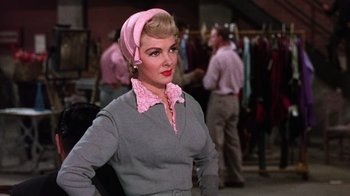 Movie still from “Kiss Me Kate” (1953), directed by George Sidney – A woman with a pink head scarf and a gray sweater; Medium shot, Low angle