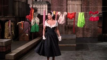 Movie still from “Kiss Me Kate” (1953), directed by George Sidney – A woman in a black dress standing in front of clothes; Wide shot, Low angle