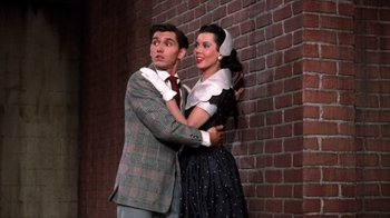 Movie still from “Kiss Me Kate” (1953), directed by George Sidney – A man and a woman standing next to a brick wall; Medium shot, Low angle