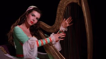 Movie still from “Kiss Me Kate” (1953), directed by George Sidney – A woman in a green and white dress playing a harp; Medium shot, Low angle
