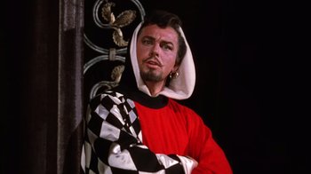 Movie still from “Kiss Me Kate” (1953), directed by George Sidney – A man in a red and black outfit with a checkered scarf; Medium shot, Low angle