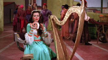 Movie still from “Kiss Me Kate” (1953), directed by George Sidney – A woman sitting in front of a harp in front of other people; Medium shot, High angle