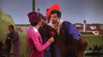 Movie still from “Kiss Me Kate” (1953), directed by George Sidney – A man dressed as a jester holding a rose in his hand and another man dressed as a jester; Medium shot, Over the shoulder angle