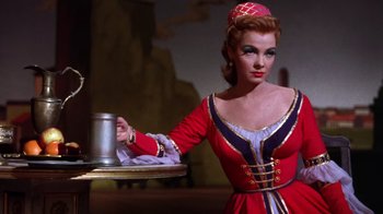 Movie still from “Kiss Me Kate” (1953), directed by George Sidney – A woman dressed in a red and black dress holding a tray of silverware; Medium shot, Low angle