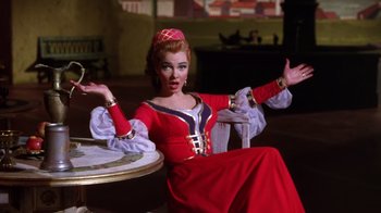 Movie still from “Kiss Me Kate” (1953), directed by George Sidney – A woman sitting at a table wearing a red dress; Medium shot, Low angle