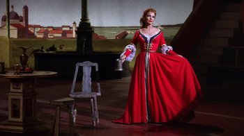 Movie still from “Kiss Me Kate” (1953), directed by George Sidney – A woman in a red dress standing in front of a chair; Wide shot, High angle