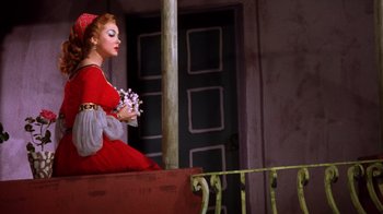 Movie still from “Kiss Me Kate” (1953), directed by George Sidney – A woman in a red dress sitting on top of a railing; Medium shot, Low angle