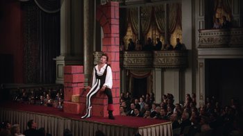 Movie still from “Kiss Me Kate” (1953), directed by George Sidney – A man is sitting on a stage in a costume; Wide shot, Low angle