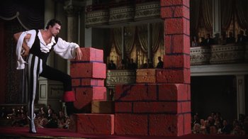 Movie still from “Kiss Me Kate” (1953), directed by George Sidney – A man is jumping over a bunch of red bricks; Wide shot, Low angle