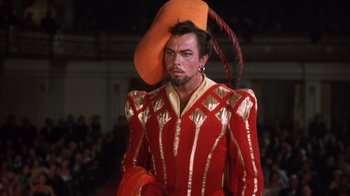 Movie still from “Kiss Me Kate” (1953), directed by George Sidney – A man in a red and gold outfit with a hat on his head; Medium shot, Low angle