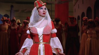 Movie still from “Kiss Me Kate” (1953), directed by George Sidney – A woman dressed in a red and white dress and a hat; Medium shot, Low angle