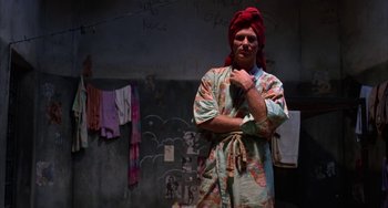 Movie still from “Kiss of the Spider Woman” (1985), directed by Hector Babenco – A man with a red turban standing next to a wall; Medium shot, Low angle