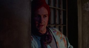 Movie still from “Kiss of the Spider Woman” (1985), directed by Hector Babenco – A man with a red turban is standing by a door; Close Up shot, Over the shoulder angle