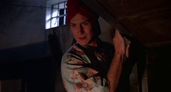 Movie still from “Kiss of the Spider Woman” (1985), directed by Hector Babenco – A man with a red turban is holding something; Close Up shot, Low angle