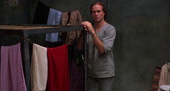 Movie still from “Kiss of the Spider Woman” (1985), directed by Hector Babenco – A man standing in front of a rack of clothes; Medium shot, Low angle