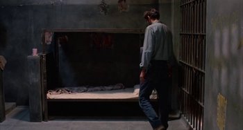 Movie still from “Kiss of the Spider Woman” (1985), directed by Hector Babenco – A man walking in a jail cell next to a bed; Wide shot, High angle
