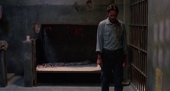 Movie still from “Kiss of the Spider Woman” (1985), directed by Hector Babenco – A man standing in front of a bed in a dimly - lit room; Wide shot, Low angle
