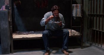 Movie still from “Kiss of the Spider Woman” (1985), directed by Hector Babenco – A man sitting on a bench eating food; Wide shot, High angle