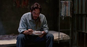 Movie still from “Kiss of the Spider Woman” (1985), directed by Hector Babenco – A man sitting on a bed with a plate of food in front of him; Medium shot, Low angle