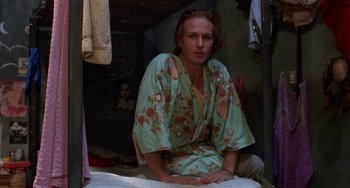 Movie still from “Kiss of the Spider Woman” (1985), directed by Hector Babenco – A man sitting on top of a bed wearing a robe; Medium shot, Low angle