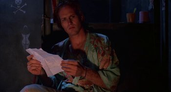 Movie still from “Kiss of the Spider Woman” (1985), directed by Hector Babenco – A man sitting on a couch holding a piece of paper; Close Up shot, Low angle