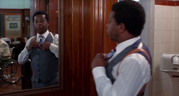 Movie still from “Kiss of the Spider Woman” (1985), directed by Hector Babenco – A man in a suit and tie looking at himself in the mirror; Medium shot, Over the shoulder angle