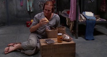 Movie still from “Kiss of the Spider Woman” (1985), directed by Hector Babenco – A man sitting on the ground with a box of food; Medium shot, High angle