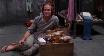 Movie still from “Kiss of the Spider Woman” (1985), directed by Hector Babenco – A man sitting on the ground next to a box of food; Medium shot, High angle