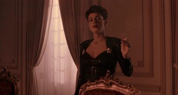 Movie still from “Kiss of the Spider Woman” (1985), directed by Hector Babenco – A woman smoking a cigarette while standing in front of a chair; Medium shot, Low angle