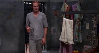 Movie still from “Kiss of the Spider Woman” (1985), directed by Hector Babenco – A man holding a cup in a jail cell; Medium shot, Low angle