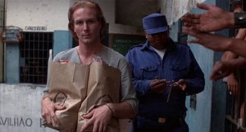 Movie still from “Kiss of the Spider Woman” (1985), directed by Hector Babenco – A man holding a paper bag while standing next to another man; Medium shot, Low angle