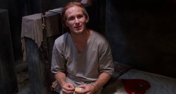 Movie still from “Kiss of the Spider Woman” (1985), directed by Hector Babenco – A man sitting on the ground holding a cigarette; Close Up shot, High angle