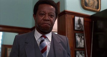 Movie still from “Kiss of the Spider Woman” (1985), directed by Hector Babenco – A man in a suit and tie standing in front of a wall; Close Up shot, Low angle