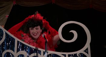 Movie still from “Kiss of the Spider Woman” (1985), directed by Hector Babenco – A woman wearing a red dress and a red hat is on a stage; Medium shot, Low angle