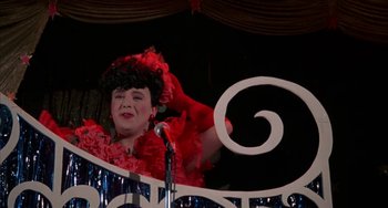Movie still from “Kiss of the Spider Woman” (1985), directed by Hector Babenco – A woman wearing a red dress and a red hat is on a stage; Medium shot, Low angle