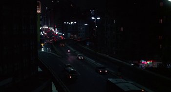 Movie still from “Kiss of the Spider Woman” (1985), directed by Hector Babenco – Cars are driving down a city street at night; Extreme Wide shot, High angle