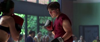 Movie still from “Kiss the Girls” (1997), directed by Gary Fleder – A man in a red shirt is boxing in a gym; Medium shot, Low angle