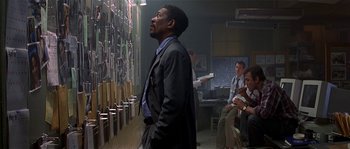 Movie still from “Kiss the Girls” (1997), directed by Gary Fleder – A man in a suit and tie standing next to a wall; Medium shot, Over the shoulder angle
