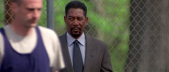 Movie still from “Kiss the Girls” (1997), directed by Gary Fleder – A man in a suit and tie standing in front of a chain link fence; Close Up shot, Over the shoulder angle