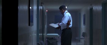 Movie still from “Kiss the Girls” (1997), directed by Gary Fleder – A man standing in a room holding a book; Medium shot, Low angle