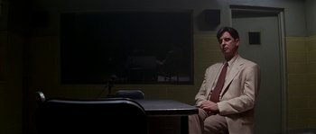 Movie still from “Kiss the Girls” (1997), directed by Gary Fleder – A man sitting in front of a microphone in front of a television; Medium shot, Low angle